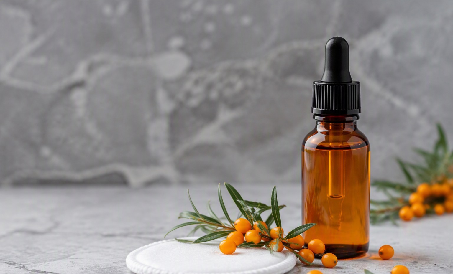 An amber dropper bottle of sea buckthorn oil with a cotton pad and fresh berries