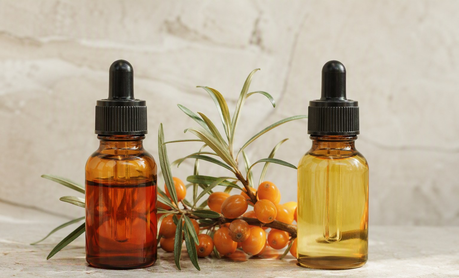 Two amber bottles of sea buckthorn oil, deep orange berry oil beside pale seed oil