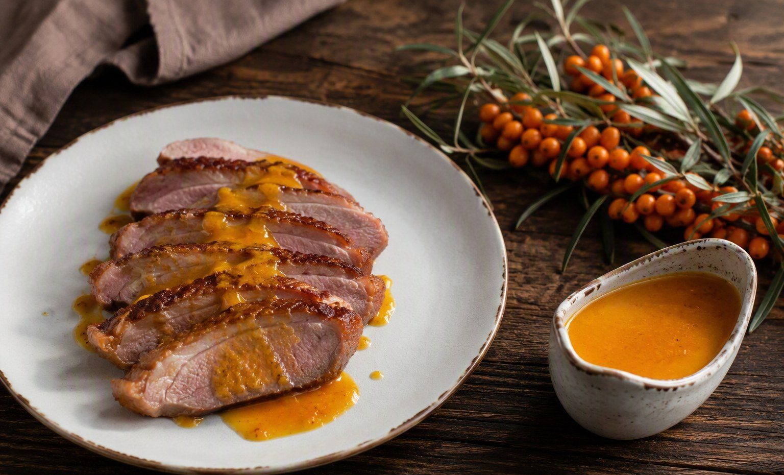 Sliced duck breast with glossy orange sea buckthorn pan sauce and a small sauce boat