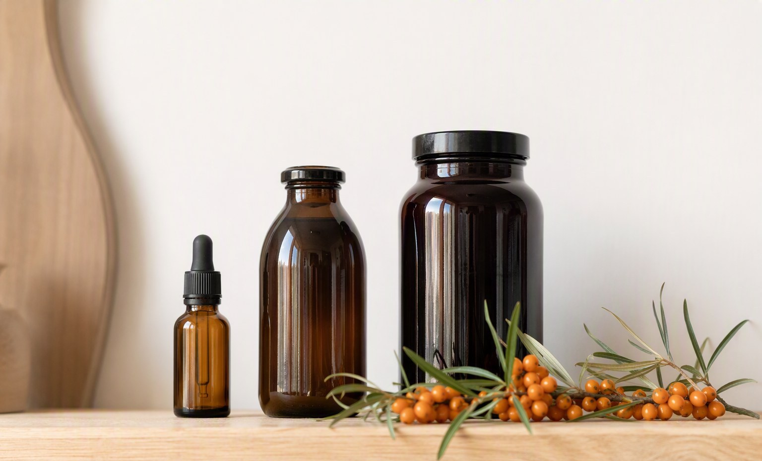 Three unbranded sea buckthorn bottles in ascending sizes on light wood with fresh berries