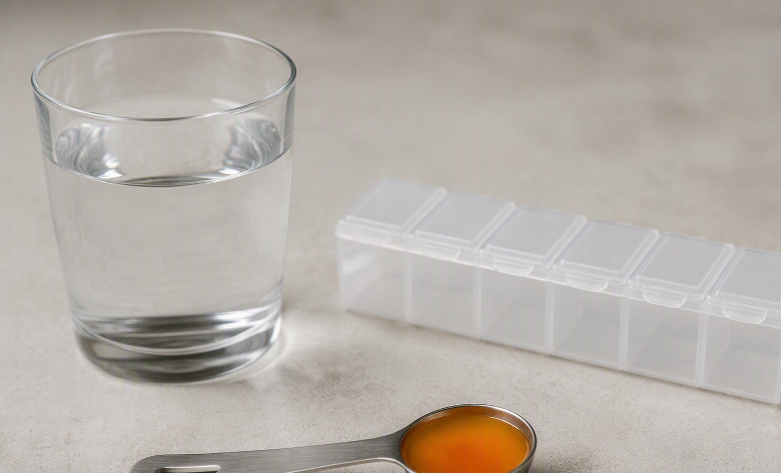 A measured spoon of sea buckthorn oil beside a glass of water and a weekly pill organizer