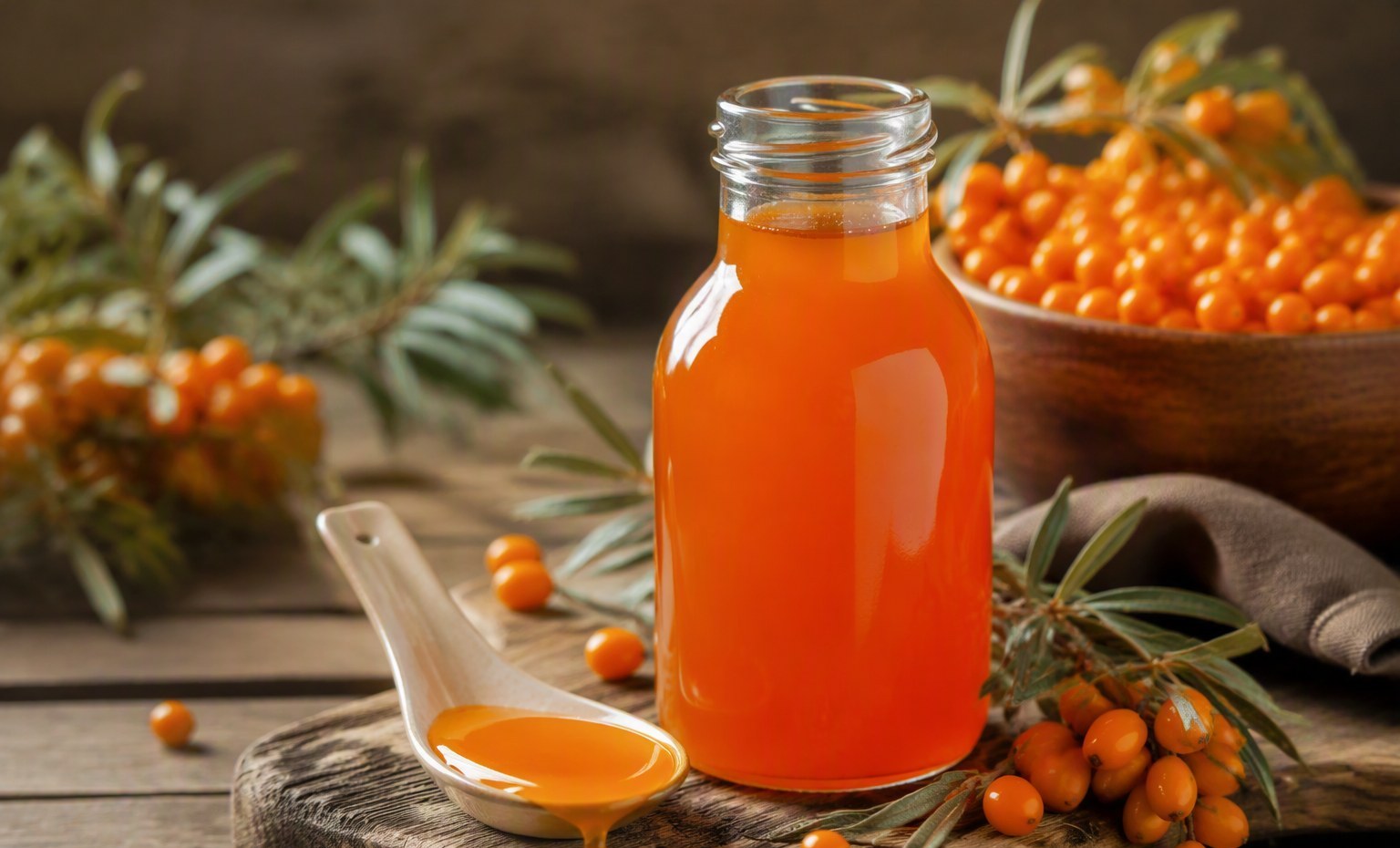 A glass bottle of bright orange sea buckthorn syrup with a drizzling spoon and fresh berries
