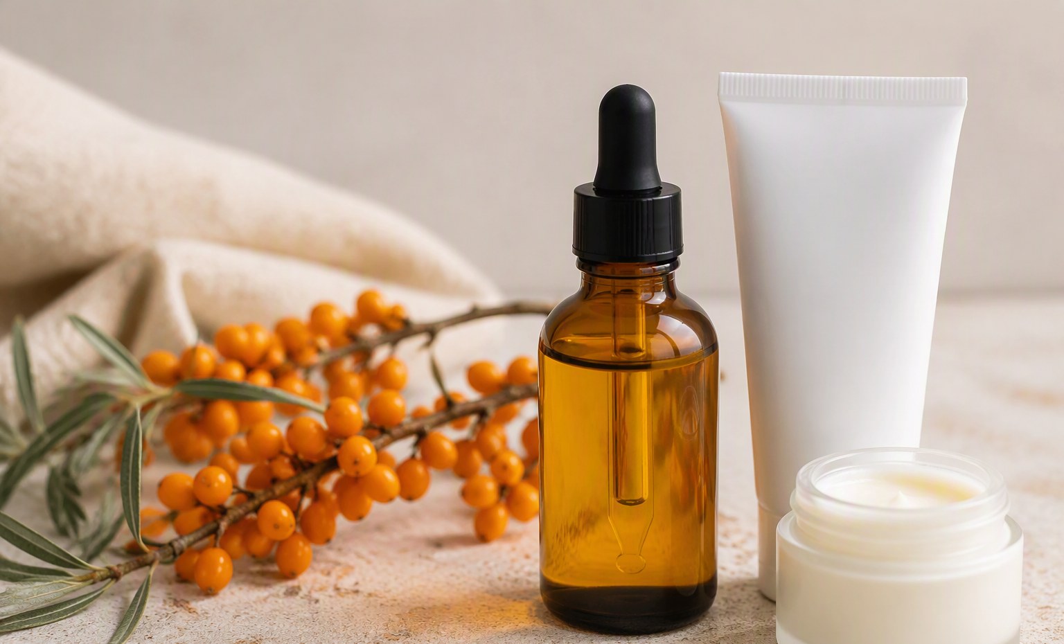 An amber bottle of sea buckthorn body oil beside a plain tube, a cream jar, and fresh berries