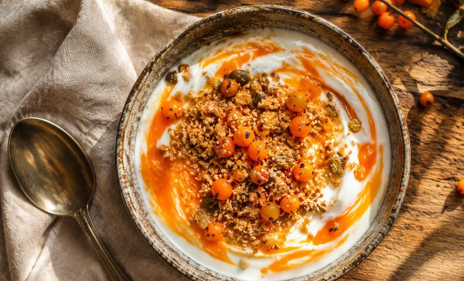 A yogurt bowl swirled with orange sea buckthorn, topped with granola and berries